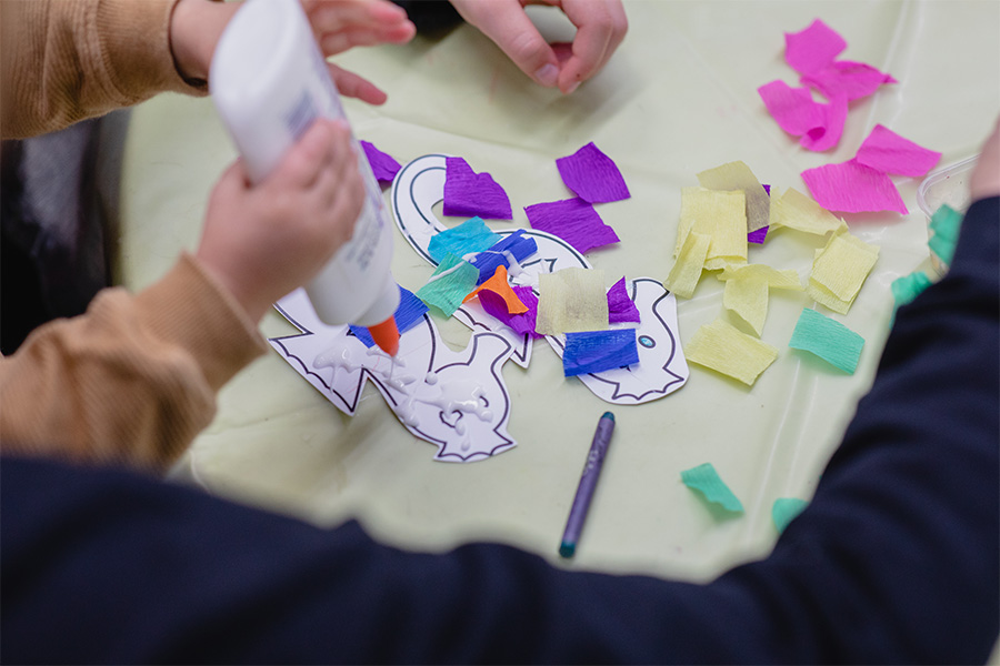 A child's hand is shown holding a bottle of glue and sqeezing the glue onto paper fish crafts